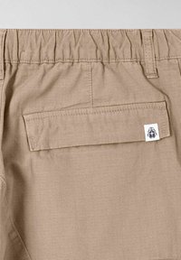 Beige shorts med elastisk talje og en enkelt baglomme. Har et lille logo-patch på lommen. Textureret stof med fin vævning.