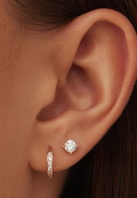 Boucles d'oreilles créoles en or rose avec des accents en pierre claire, accompagnées d'une boucle d'oreille claire ronde. Vue en gros plan de l'oreille.