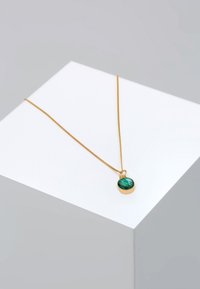 Collier en or avec une fine chaîne et un pendentif rond en malachite verte présentant des motifs texturés. Le pendentif est entouré d'un godron en or.