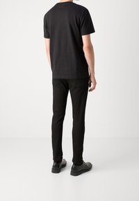 Czarny bawełniany t-shirt z krótkim rękawem, w zestawieniu z czarnymi dopasowanymi dżinsami i błyszczącymi czarnymi butami. Dżinsy mają tylne kieszenie.