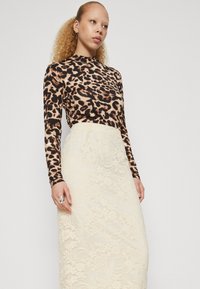 Leopardskinn mønstret langermet topp i beige og svart, kombinert med en kremfarget blyantskjørt i blonde med blomstermønster og en figursydd silhuett.