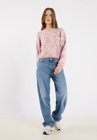 Fargerik strikket genser med lange ermer, som har et gradientmønster i rosa, gult og blått. Brukt med lyseblå baggy jeans og sneakers.