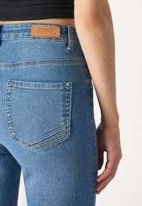 Jeans de denim azul con un parche de cuero en la parte trasera marcado "ONLY", con dos bolsillos traseros y detalles de costura estándar.