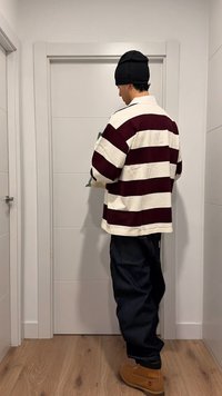 Chemise en coton à rayures horizontales rouges et blanches, coupe décontractée, associée à un jean ample foncé et des bottes de travail couleur beige, debout devant une porte.