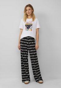 T-shirt blanc avec un graphique coloré "New York", associé à un pantalon large noir à pois blancs. Chaussures décontractées visibles.