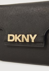 Juodas tekstūruotas rankinukas su auksiniu "DKNY" logotipo aksesuaru, pasižymintis elegantišku dizainu ir švariomis linijomis, tinkamas įvairioms progoms.