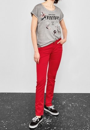 Camiseta gráfica gris de manga corta con diseño de texto, combinada con pantalones rojos de corte slim y zapatillas negras con cordones blancos.
