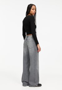 Schwarzes, langärmliges Cropped-Top kombiniert mit grauen, weit geschnittenen, hoch taillierten Jeans, die über zwei Gesäßtaschen und einen strukturierten Stoff verfügen.
