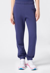 Pantalones deportivos morados con cintura y puños elásticos, hechos de un material suave. Combinados con zapatillas blancas con acentos en rosa y azul.