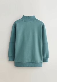 Mėlynas medvilninis džemperis su aukštu apykakle, nukritusiais pečiais, raukšlėtomis rankogaliais ir apačia, su lygia, šiek tiek tekstūruota paviršiumi.