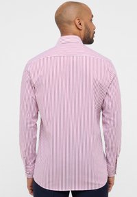 Camicia a maniche lunghe con sottili righe rosse e bianche, colletto classico, polsini con bottone e orlo curvo. Materiale in cotone.