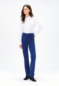 Blauwe katoenen rechttoe rechtaan broek met voorzakken, gecombineerd met een witte blouse met kraag en zwarte enkelhakschoenen. Eenvoudig en op maat gemaakt ontwerp.