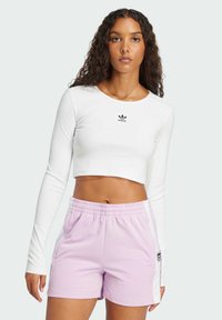 White long-sleeve crop top with a black Adidas logo, paired with pink athletic shorts featuring white side stripes and an elastic waistband.