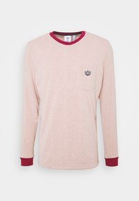 Långärmad ljus rosa Adidas-tröja med röd krage och muddar, liten svart Adidas trefoil-logga på bröstfickan.