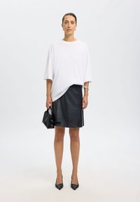 Hvid oversized t-shirt, sort læder A-line nederdel, sort håndtaske og spidse sorte hæle. Minimalistisk design, glatte teksturer.