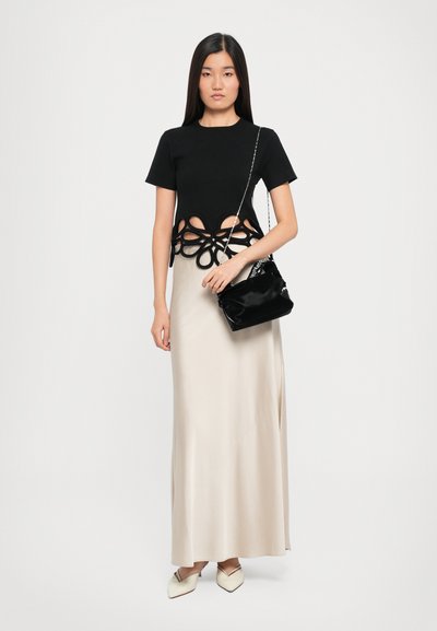 Black cropped t-shirt with cut-out floral design, paired with a sleek beige satin maxi skirt. Model holds a small black shoulder bag.
