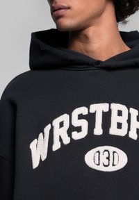 Felpa nera con cappuccio e logo ricamato bianco "WRSTBH" e dettagli. Presenta un cappuccio consumato e un tessuto morbido e textured.