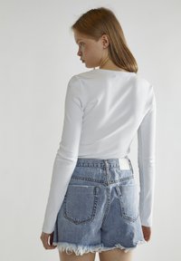 Top blanco de manga larga con tejido acanalado, combinado con pantalones cortos de mezclilla azul claro con dobladillos deshilachados y bolsillos traseros. Diseño sencillo con una silueta ajustada.