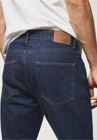 Vaqueros de mezclilla azul oscuro con una textura suave, que cuentan con dos bolsillos traseros y una etiqueta de cuero en la cintura.