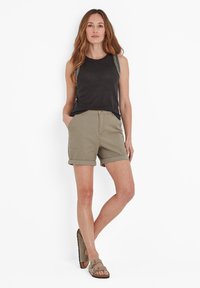 Black tank top with decorative straps, paired with olive green rolled shorts and brown sandals, showcasing a casual outfit.
