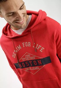 Czerwona bluza z kapturem z bawełny z graficznym nadrukiem z przodu. Posiada regulowany kaptur oraz kieszeń kangurzą. Widoczny napis "BOSTON".