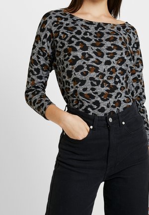 Haut à manches longues en imprimé léopard, présentant des couleurs grises, noires et brunes ; tissu doux, coupe décontractée, encolure bateau, associé à un jean noir.