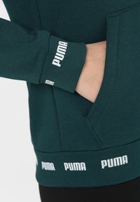 Tyrkysová mikina se žebrovanými manžetami a spodním lemem. Bílé akcenty loga "PUMA" na manžetách a spodním lemu. Vyrobena z měkké, strukturované tkaniny.