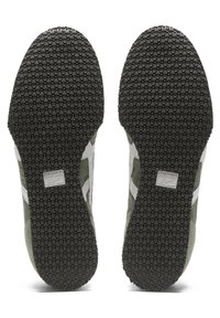 Zelené podešve tenisek mají strukturovaný gumový povrch s malými kruhovými gripy. Po straně jsou viditelné bílé detaily a logo.