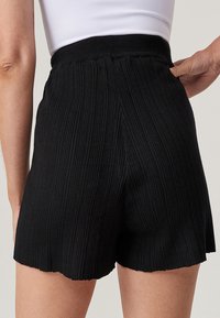Svart ribbad strumpbyxor med en bred midja, prydd med en scalloped nederkant och ett texturerat, elastiskt material för komfort.