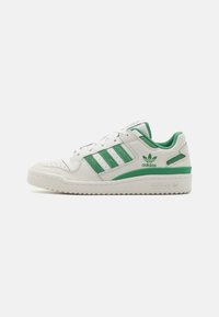 White sneaker with green accents. Features leather upper, three striped design, perforations on the toe, and textured rubber sole.