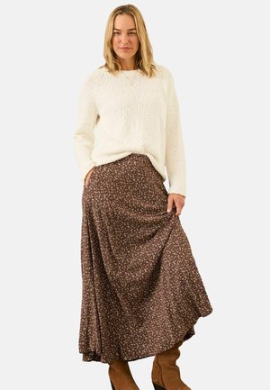 Knit sweater in cream paired with a brown floral maxi skirt. The skirt features a flowy design and pockets. Knee-high brown boots complete the look.