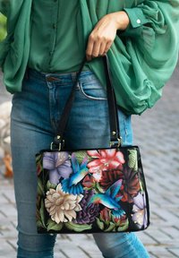 Zwarte handtas met levendige bloemen- en kolibrie- borduursels. Heeft stevige zwarte handvatten en een gestructureerde vorm.