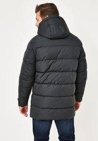 Schwarze Puffjacke mit Kapuze, ausgestattet mit gesteppte Abschnitten. Der Rücken zeigt eine glatte Textur und ein leicht verlängertes Design.
