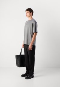 Grå t-skjorte med korte ermer, svarte vide bukser, svarte lærssko, bærer en svart lær tote bag. Enkelt og rent design.