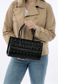 Black quilted handbag with smooth leather accents and structured shape. Features dual handles and a sleek design, held by a person.
