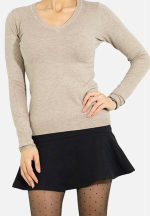 Pull beige à manches longues et décolleté en V, associé à une jupe noire évasée et des collants à pois, présentant une texture lisse et une coupe ajustée.