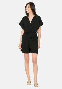 Czarny kombinezon z krótkimi rękawami, o kroju kopertowym i wiązaniu w talii, wykonany z lekkiego materiału. Posiada dekolt w kształcie litery V oraz luźny krój.