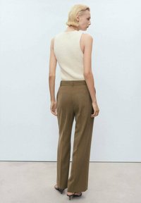 Beige ärmlös stickad topp kombinerad med högmidjade, vida bruna byxor. Slät tygtextur och minimalistisk design utan synliga mönster.