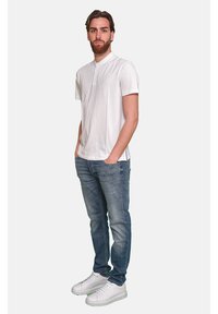 Polo bianco a maniche corte con pattina abbottonata, abbinato a jeans in denim blu e scarpe da ginnastica bianche. Design semplice, vestibilità casual.