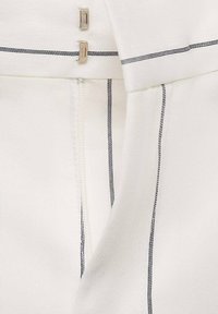 Bílý materiál s jemnými tmavě modrými pruhy, s uzávěrem na zip a kovovými akcenty, zdůrazňující strukturovaný design a texturu.