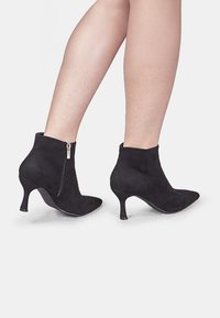 Bottines en suède noir avec bouts pointus, fermeture éclair sur le côté et talons de 4 cm, présentant une texture lisse et mate ainsi qu'une silhouette élancée.
