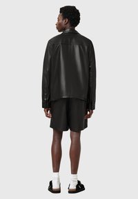 Schwarze Lederjacke mit einer glatten Textur, mit einem klassischen Kragen und geradem Schnitt, kombiniert mit schwarzen Shorts und Sandalen.