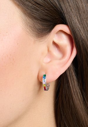 Nahaufnahme eines durchstochenen Ohrs mit einem silbernen Creolen-Ohrring, der vertikal angeordnete rechteckige, mehrfarbige Edelsteine trägt.