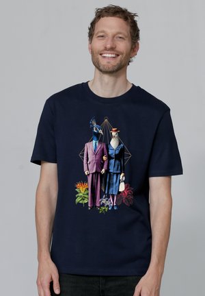 Marineblauwe katoenen t-shirt met een grafiek van twee antropomorfe vogels in pakken, omringd door kleurrijke tropische planten en geometrische lijnen.