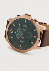 Men’s wristwatch with rose gold case, dark green dial, brown leather strap, and multiple subdials showing day, date, and 24-hour time.
