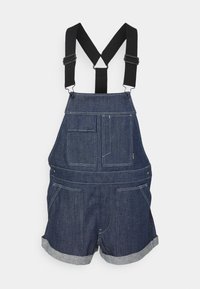 Jeanové kombinézy s nastavitelnými černými ramínky, několika kapsami, volným střihem a ohrnutými lemy. Tmavě modrá látka se viditelnými švy.