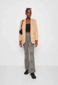 Beige blazer, svart crop top, strukturerte bukser med svart og hvit mønster, og svarte ankelstøvler. Tilbehør inkluderer en liten håndveske.