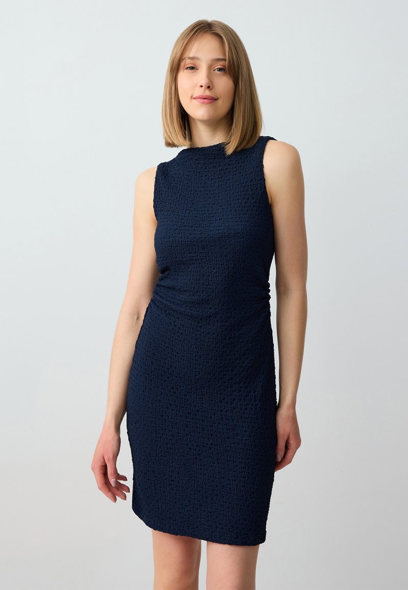 Navy blue sleeveless dress with textured fabric, round neckline, and gathered detailing on the side. Short, fitted design.