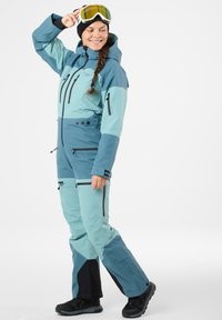 Ski suit in light blue and teal with black accents, featuring a hood, multiple zippered pockets, and a relaxed fit for mobility.