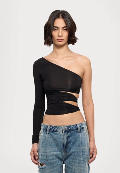 Black asymmetrical top with one long sleeve, twisted design, and cutouts at the waist. Paired with distressed blue denim jeans.
